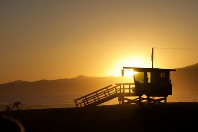 Silhouette lifeguard hut on beach against sky during sunset