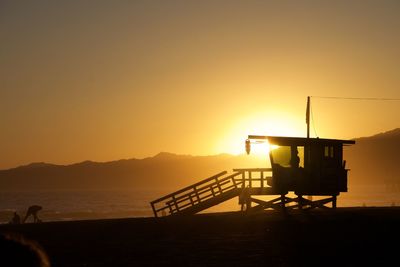 Silhouette lifeguard hut on beach against sky during sunset