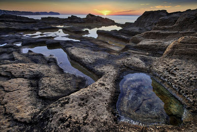 Rock formation on beach against sky during sunset