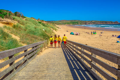 Rear view of people at beach against clear blue sky