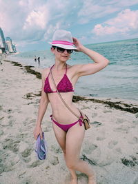 Full length portrait of beautiful woman standing on beach against sky