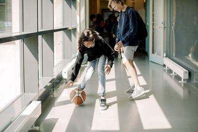 Smiling male students playing with basketball in school corridor