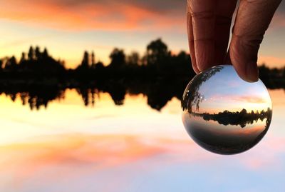 Reflection of person hand on water in lake during sunset