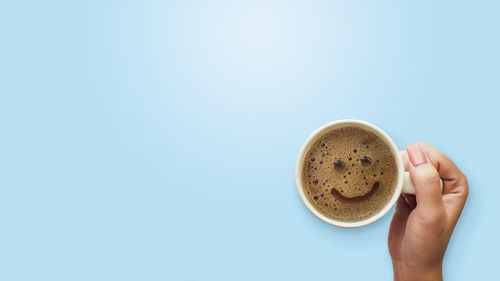 Directly above shot of hand holding coffee cup against clear blue sky