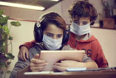 Low angle view of brothers wearing masks using digital tablet on table