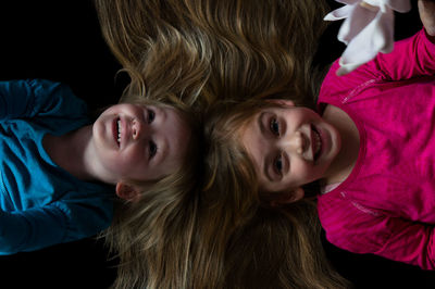 Directly above view of cheerful girls with blond hair lying on black background