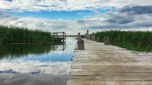 Wooden pier on lake against cloudy sky