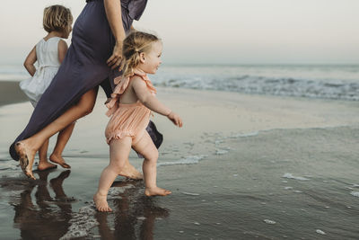 Side view of toddler girl running into the ocean at sunset