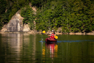 Man sitting in boat on lake against trees