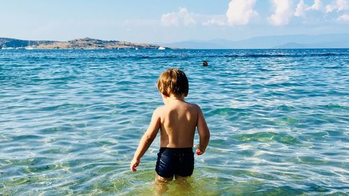 Rear view of shirtless boy standing in sea against sky