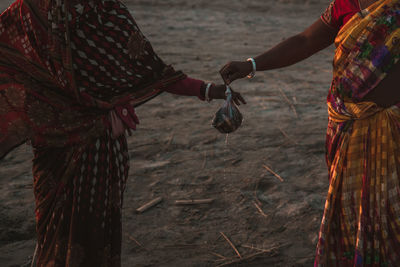 Midsection of woman giving fish in plastic bag to female friend on field