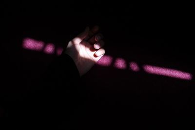 Close-up of hand touching illuminated light over black background