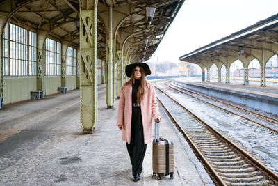 Young woman with suitcase on platform of station. traveler girl waiting