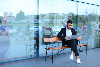 Businessman using digital tablet while sitting on bench outdoors