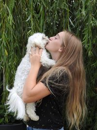 Woman kissing dog against plants