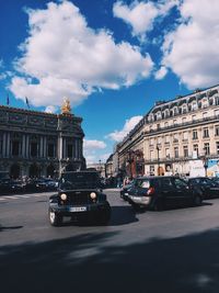 Cars on road by buildings against cloudy sky