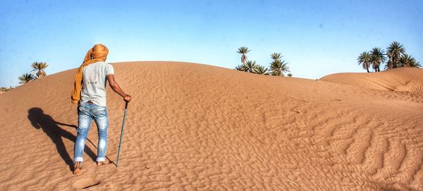 Rear view of man walking on sand dune at desert
