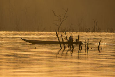 Silhouette man in boat on lake during sunset