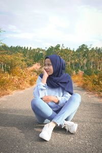 Portrait of young woman sitting on plant against sky