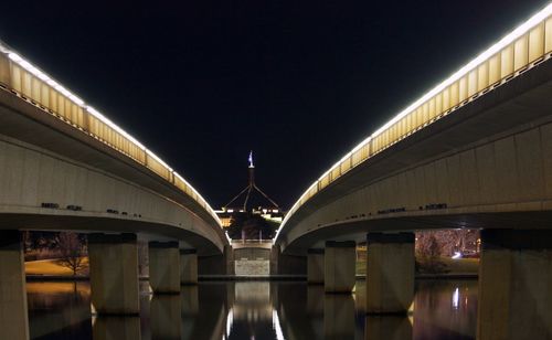 Illuminated bridge over river against sky at night