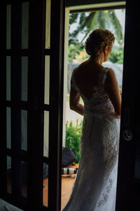 Rear view of woman looking through window at home
