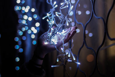 Close-up of human hand holding illuminated lighting equipment in darkroom