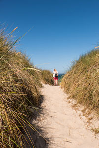 Rear view of woman standing on sand against sea and sky