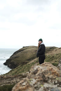 Rear view of man standing on rock by sea against sky