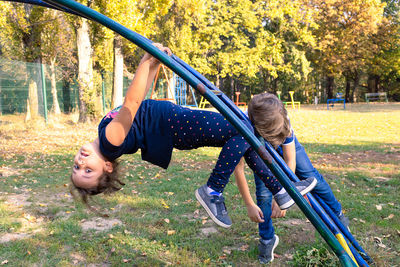 Portrait of girl hanging on play equipment with brother at park