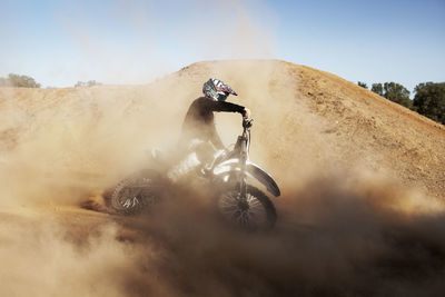 Man riding dirt bike on sand against sky