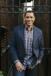 Portrait of confident smiling man leaning on metal gate