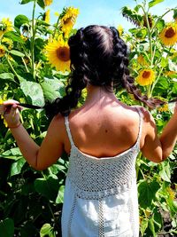 Rear view of girl standing against blooming sunflowers