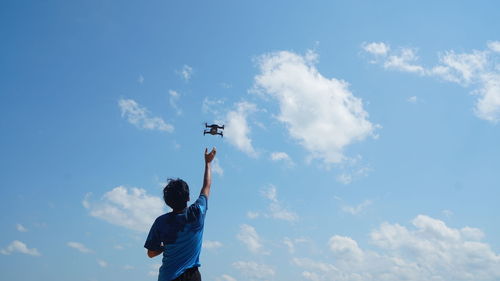 Low angle view of man flying drone against sky