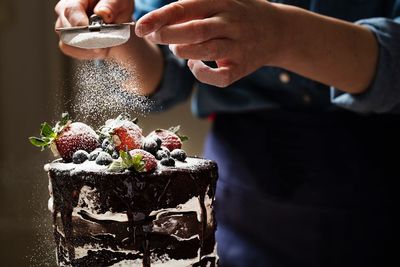 Midsection of woman sprinkling powdered sugar on cake
