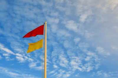 Low angle view of a red and a yellow flags against sky