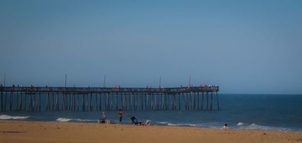 People on pier at beach against clear sky