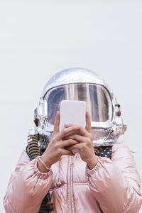 Girl with space helmet using mobile phone against wall