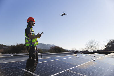 Mature technician flying drone standing by solar panel