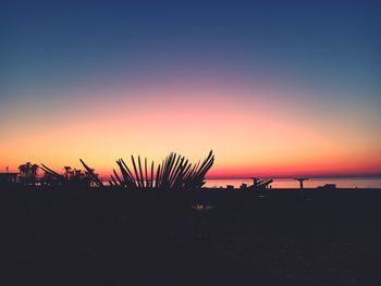 Silhouette plants by sea against romantic sky at sunset