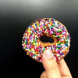 Cropped hand holding donut with colorful sprinkles