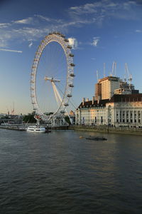 Ferris wheel by river against sky in city