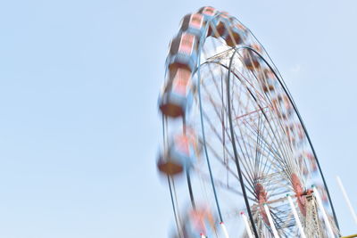 Low angle view of moving ferris wheel against clear sky
