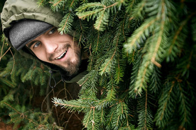 Mid adult man looking away while standing by pine tree
