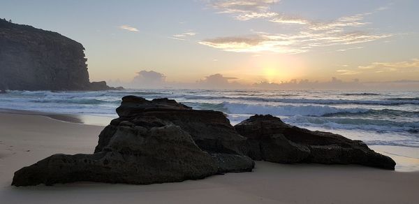 Rock formation on beach against sky during sunset