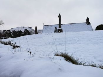 Snow covered field by building against sky