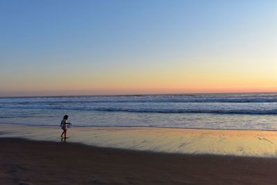 Silhouette woman walking at beach against clear sky during sunset