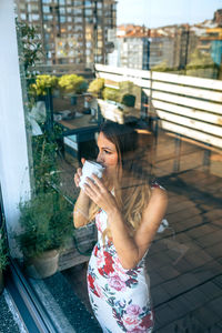 Side view of young woman holding camera while standing outdoors