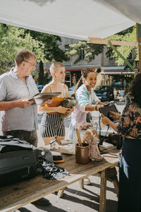 Customers talking with female stall owner while shopping at flea market