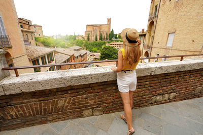 Seen from behind of beautiful tourist woman visiting old italian town. full length.