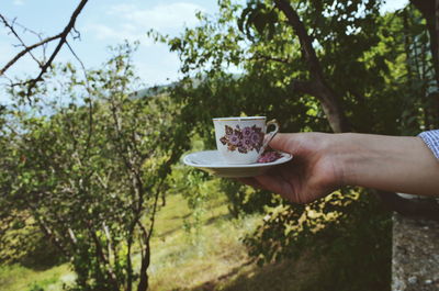 Man holding coffee cup against trees